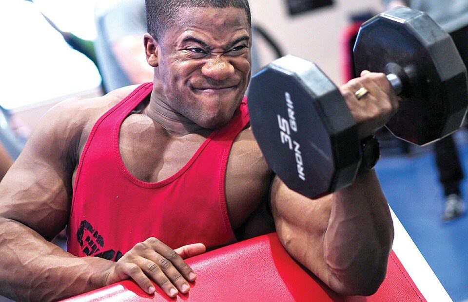 athletic man doing preacher curls with his left arm with a 35 pound dumbbell