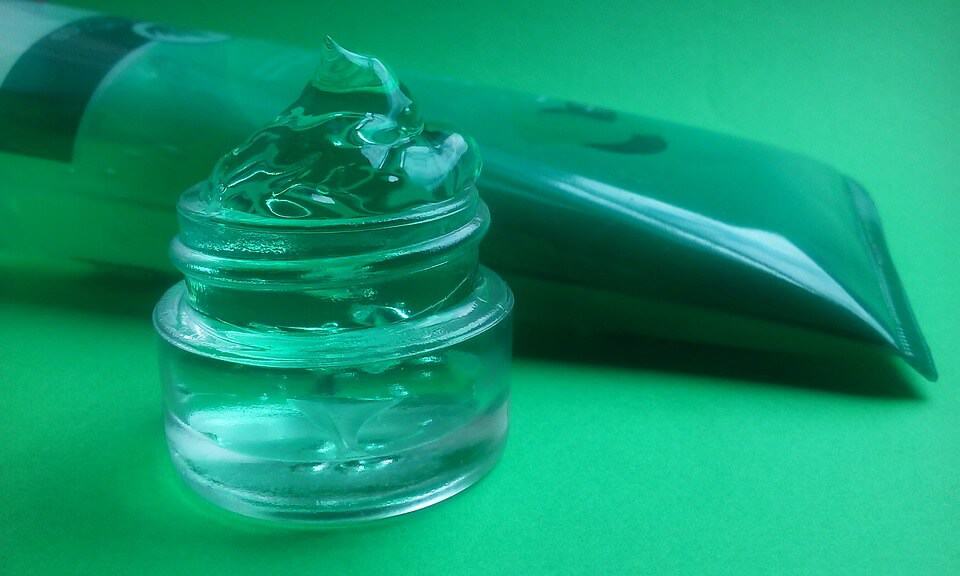 aloe vera inside small container and plastic tub, on top of a green surface